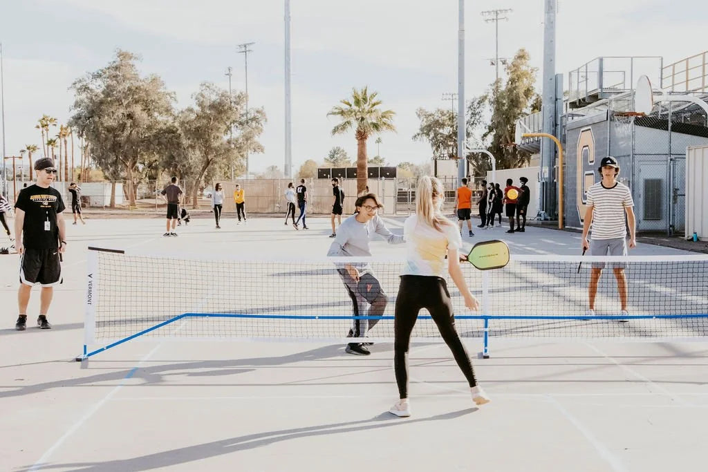 Teenagers playing pickleball on an outdoor court during a coaching session