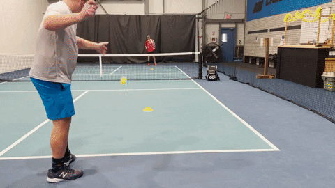 Two players practicing a pyramid-style pickleball drill on an indoor court with cones marking drill positions