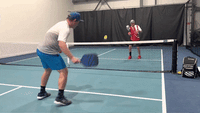 Two players practicing cooperative dink volleys at the net on an indoor pickleball court