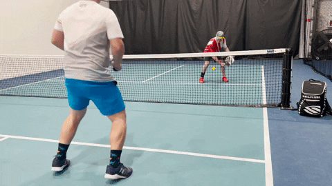 Two pickleball players at the net practicing a dink-and-flick drill on an indoor court
