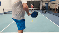 Player volleying a deep drive from the non-volley zone on an indoor pickleball court