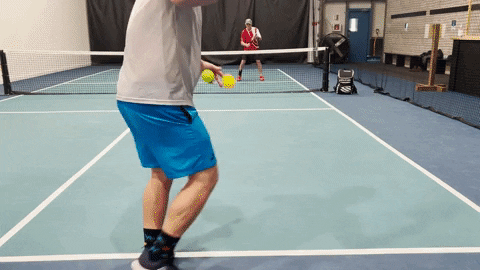 Two pickleball players practicing a drop-to-volley rally on an indoor court