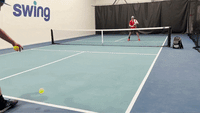 Player executing a drop volley off an incoming drive at the net on an indoor pickleball court