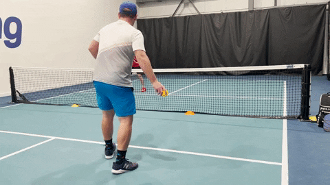 Pickleball player practicing paddle-free dinking near the net on an indoor court