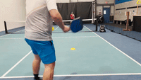 Player returning a serve deep to the opponent's baseline on an indoor pickleball court