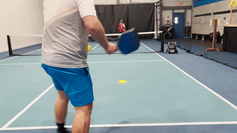 Player returning a serve deep to the opponent's baseline on an indoor pickleball court