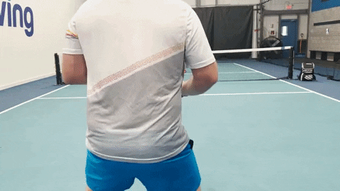 Two players demonstrating a singles pickleball drill on an indoor court, focusing on third-shot approach and court positioning