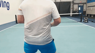 Two players demonstrating a singles pickleball drill on an indoor court, focusing on third-shot approach and court positioning
