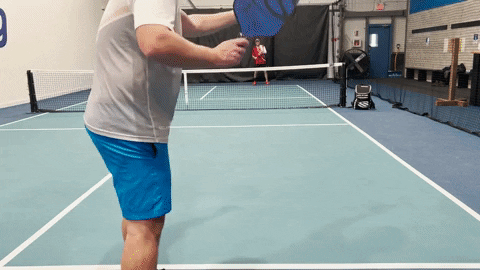 Pickleball player hitting a forehand drive from the baseline toward the net on an indoor court