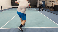 Pickleball player volleying at the net returning a driven shot on an indoor court